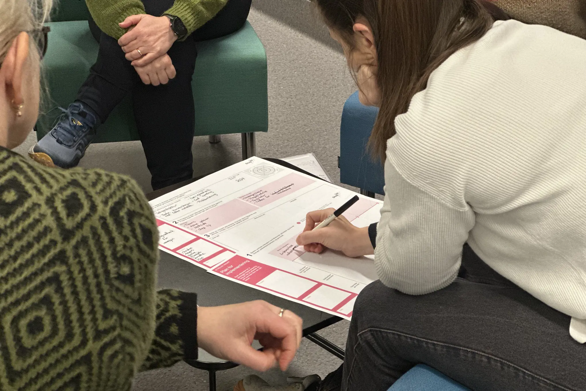 Person som skriver på et ark, med personer som sitter rundt