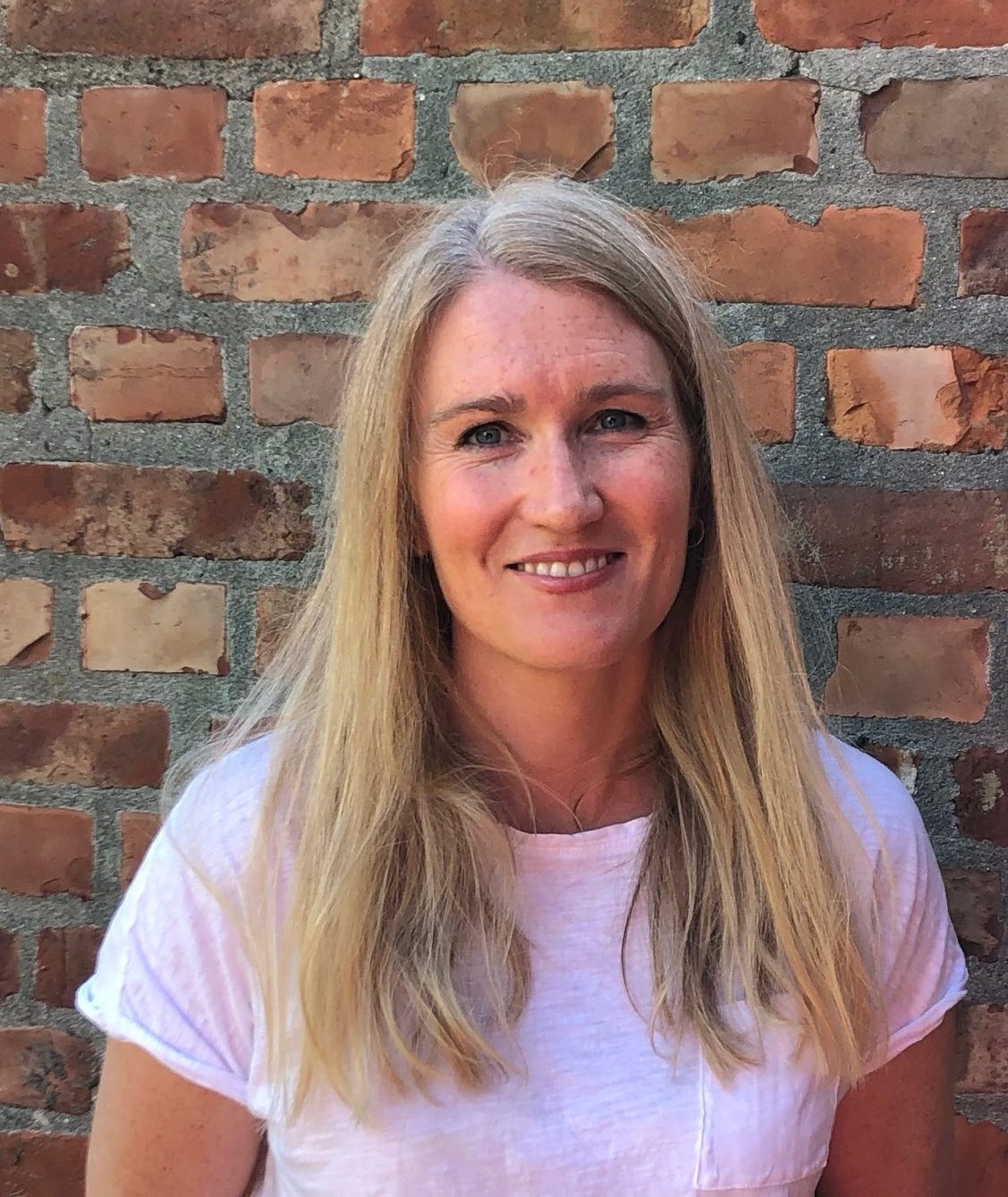 En person som smiler foran en murvegg