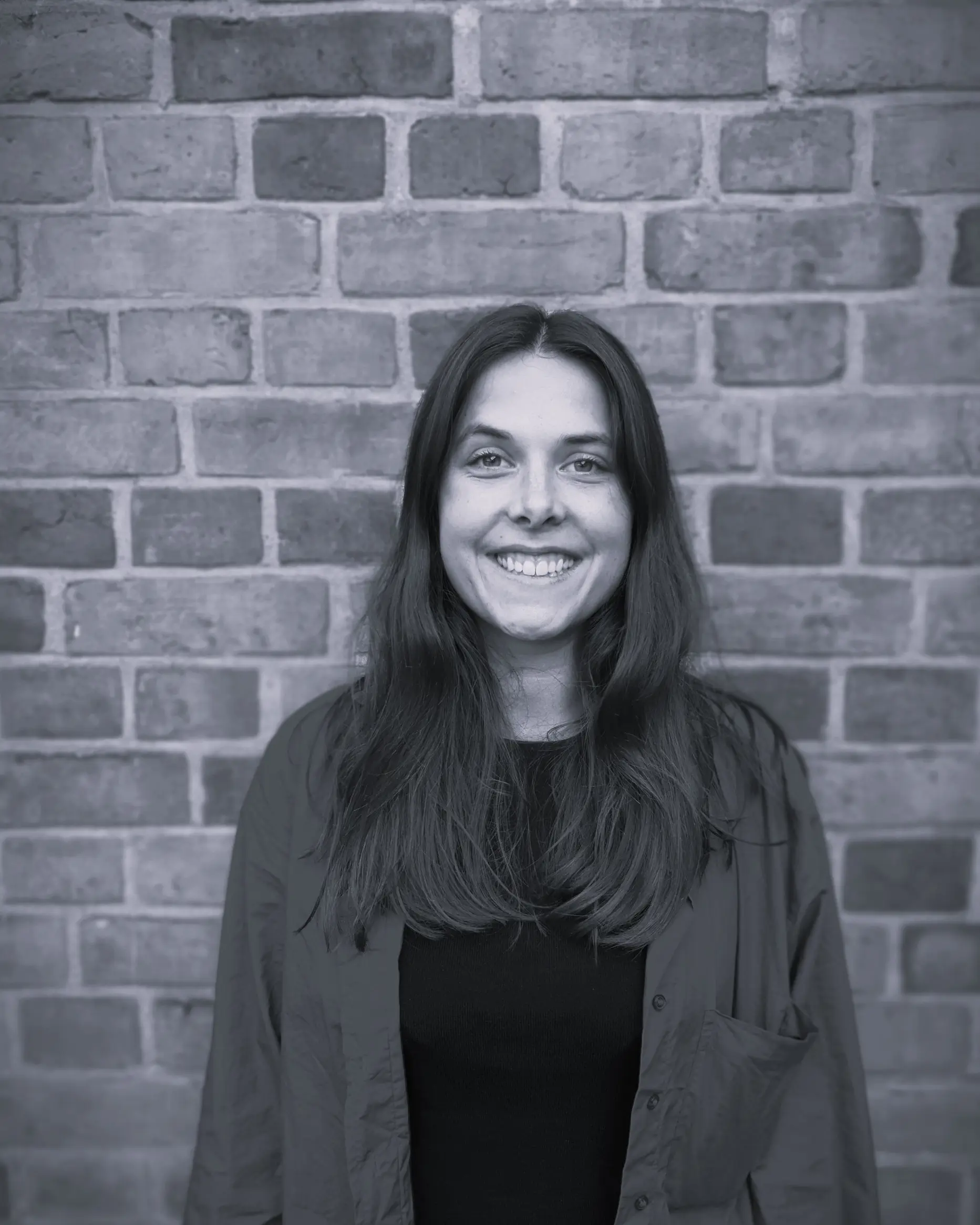 En kvinne som smiler foran en murvegg