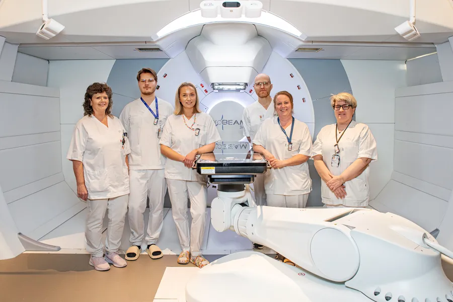 Gruppebilde av ansatte foran en protonterapimaskin