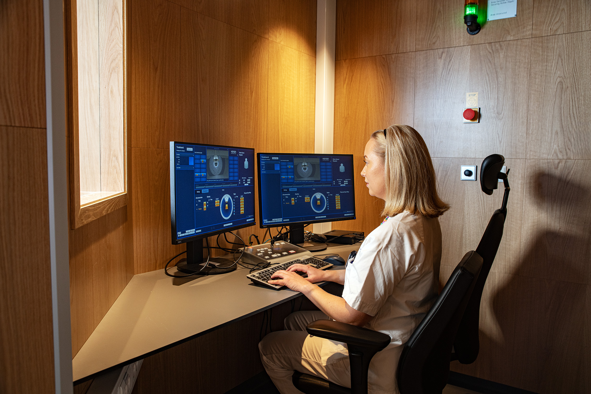 Kvinnelig ansatt sitter ved en pc som kontrollerer protonterapimaskinen