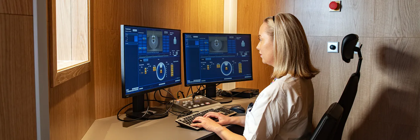 Kvinnelig ansatt sitter ved en pc som kontrollerer protonterapimaskinen