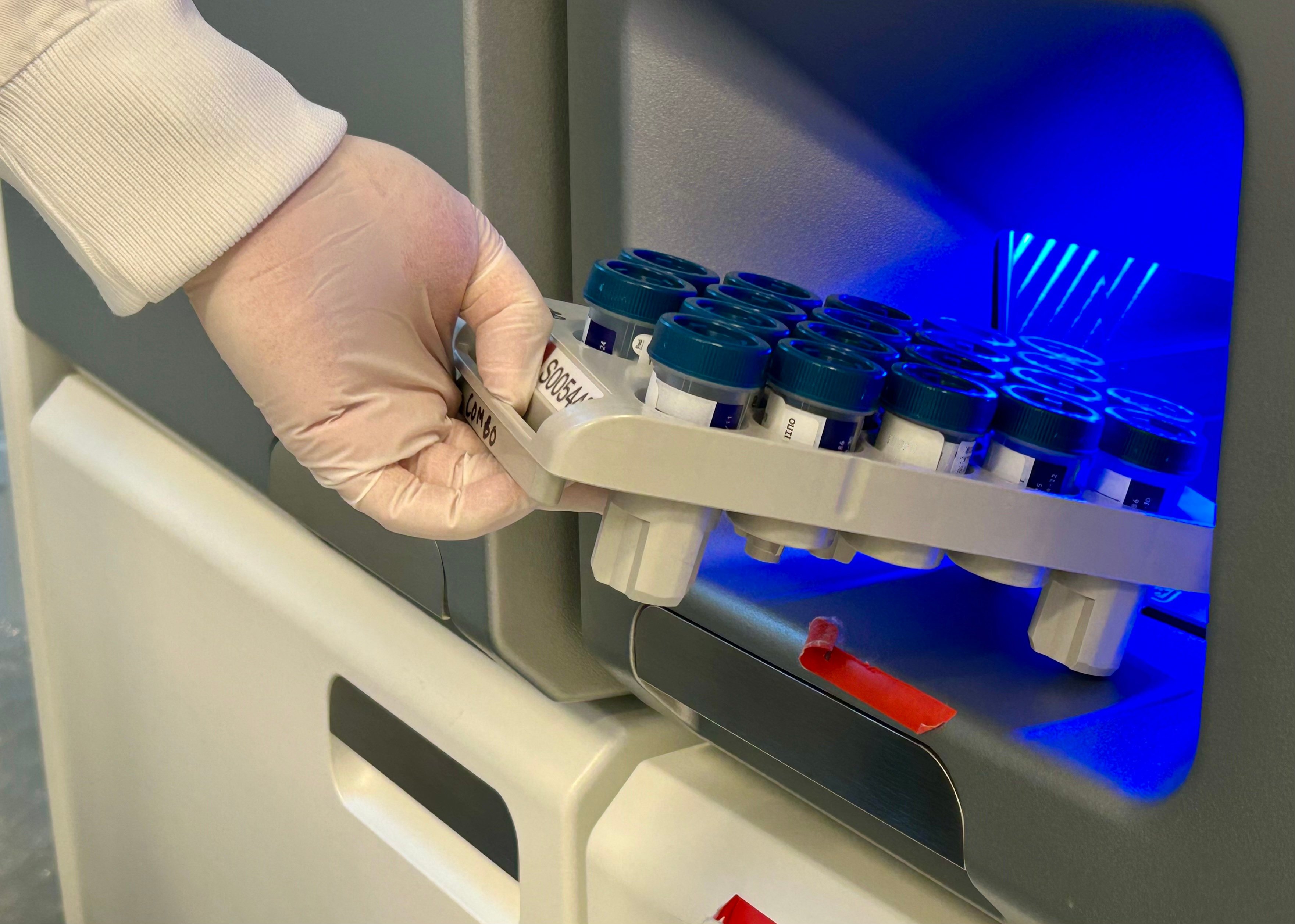 En hånd med hanske som holder et brett med reagensrør