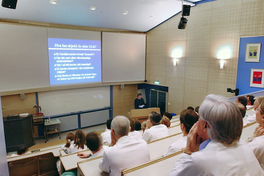 A group of people in white coats attend a lecture in an auditorium