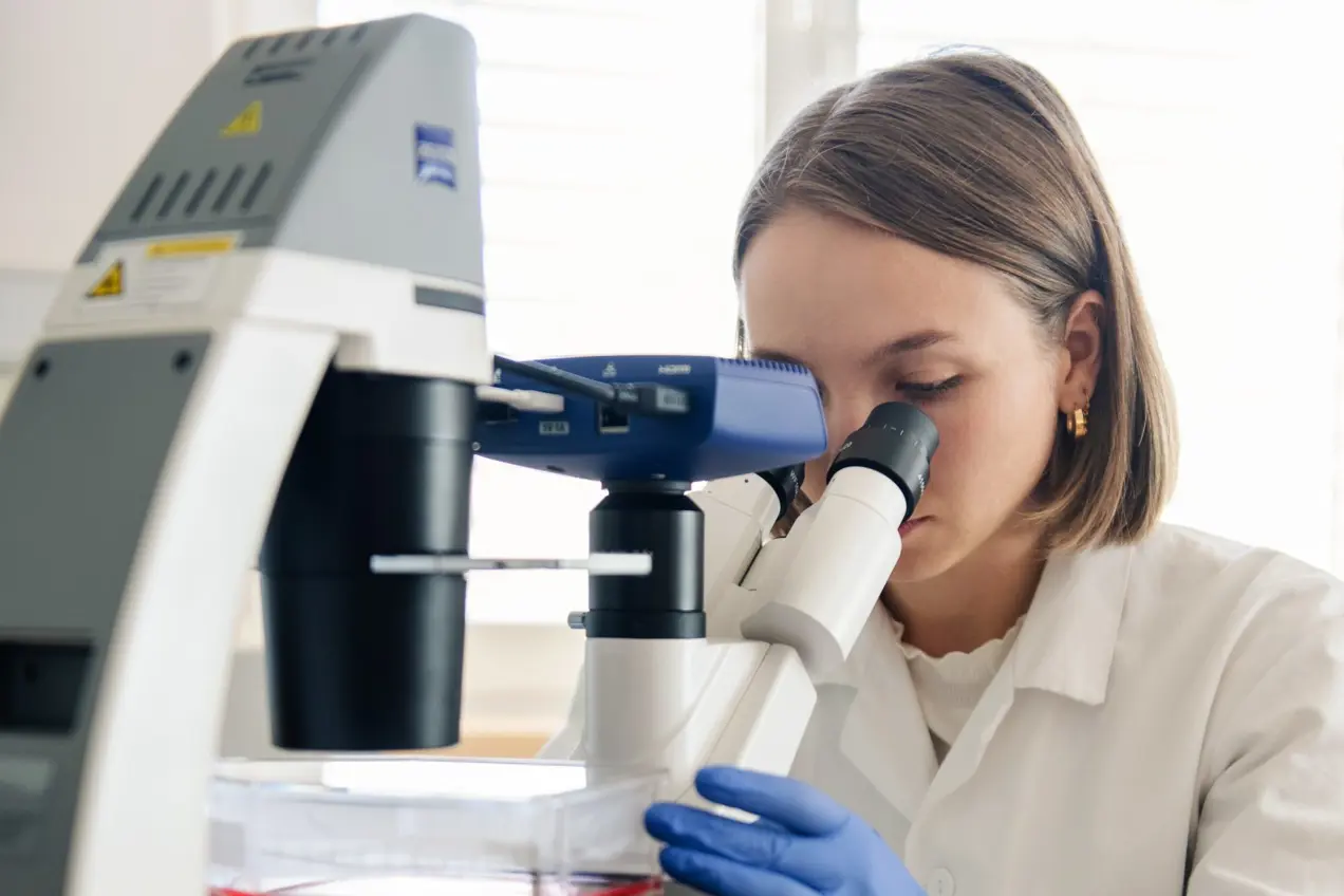 En person i laboratoriefrakk som ser gjennom et mikroskop