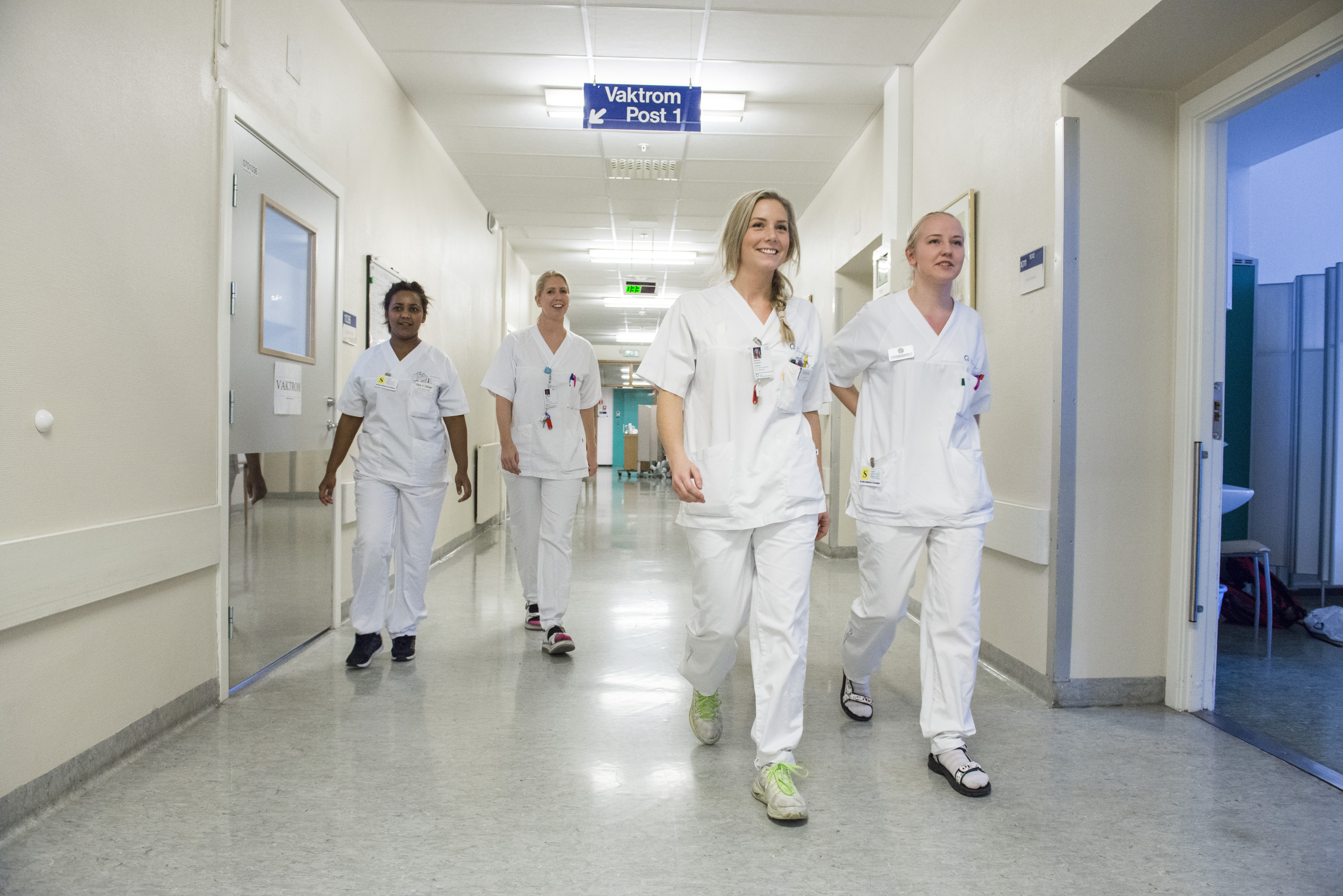 Fire fagfolk kledd i hvitt går nedover en sykehuskorridor.
