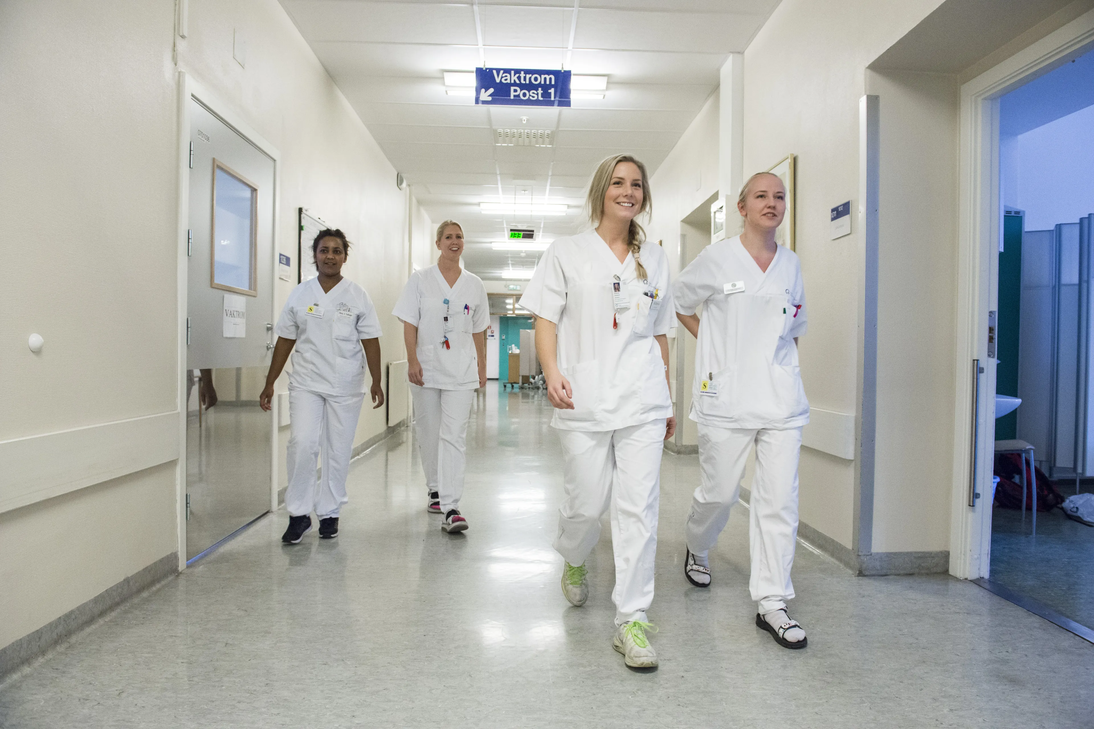 Fire fagfolk kledd i hvitt går nedover en sykehuskorridor.