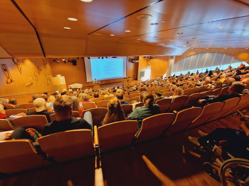 A group of people sitting in a room with a large screen