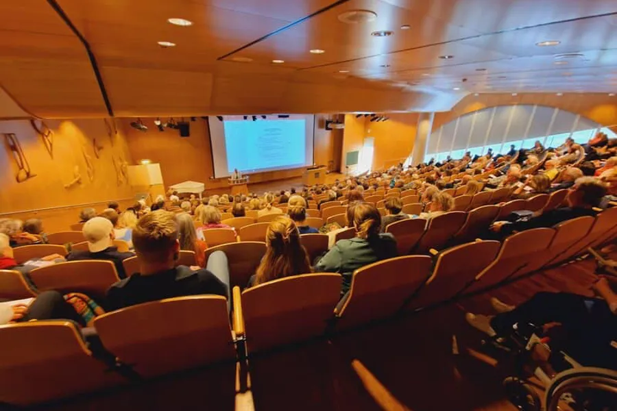 A group of people sitting in a room with a large screen