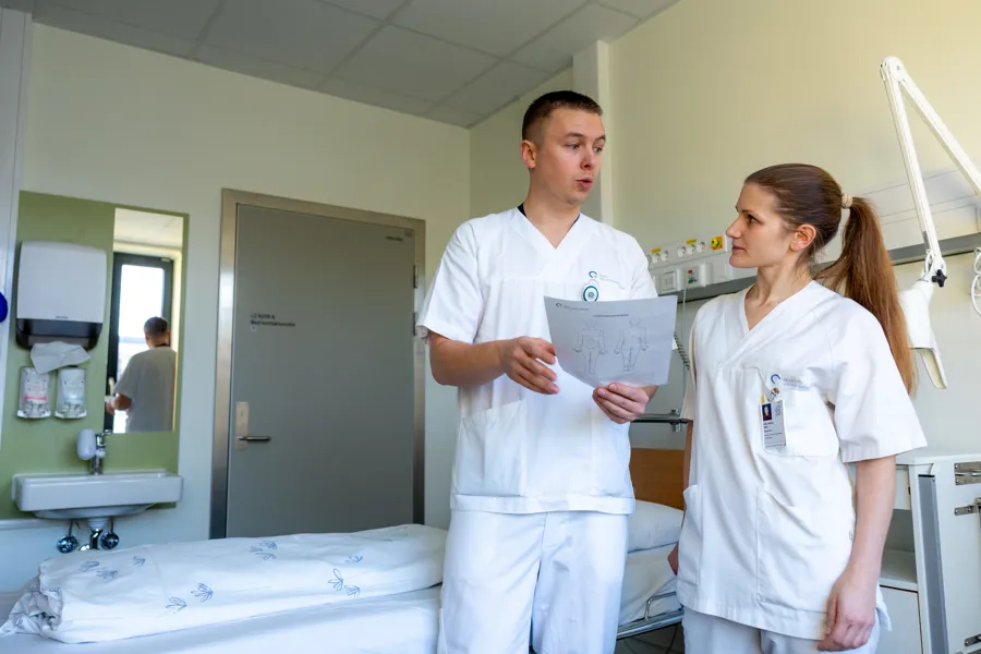 to sykepleiere i hvitt prater sammen med et ark i hånden