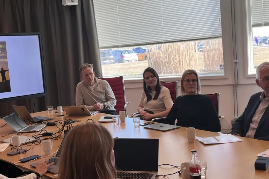 En gruppe mennesker som sitter rundt et bord med en projektorskjerm