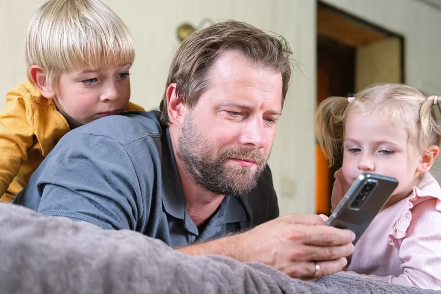 En mann som holder en telefon med to barn som ser på ham