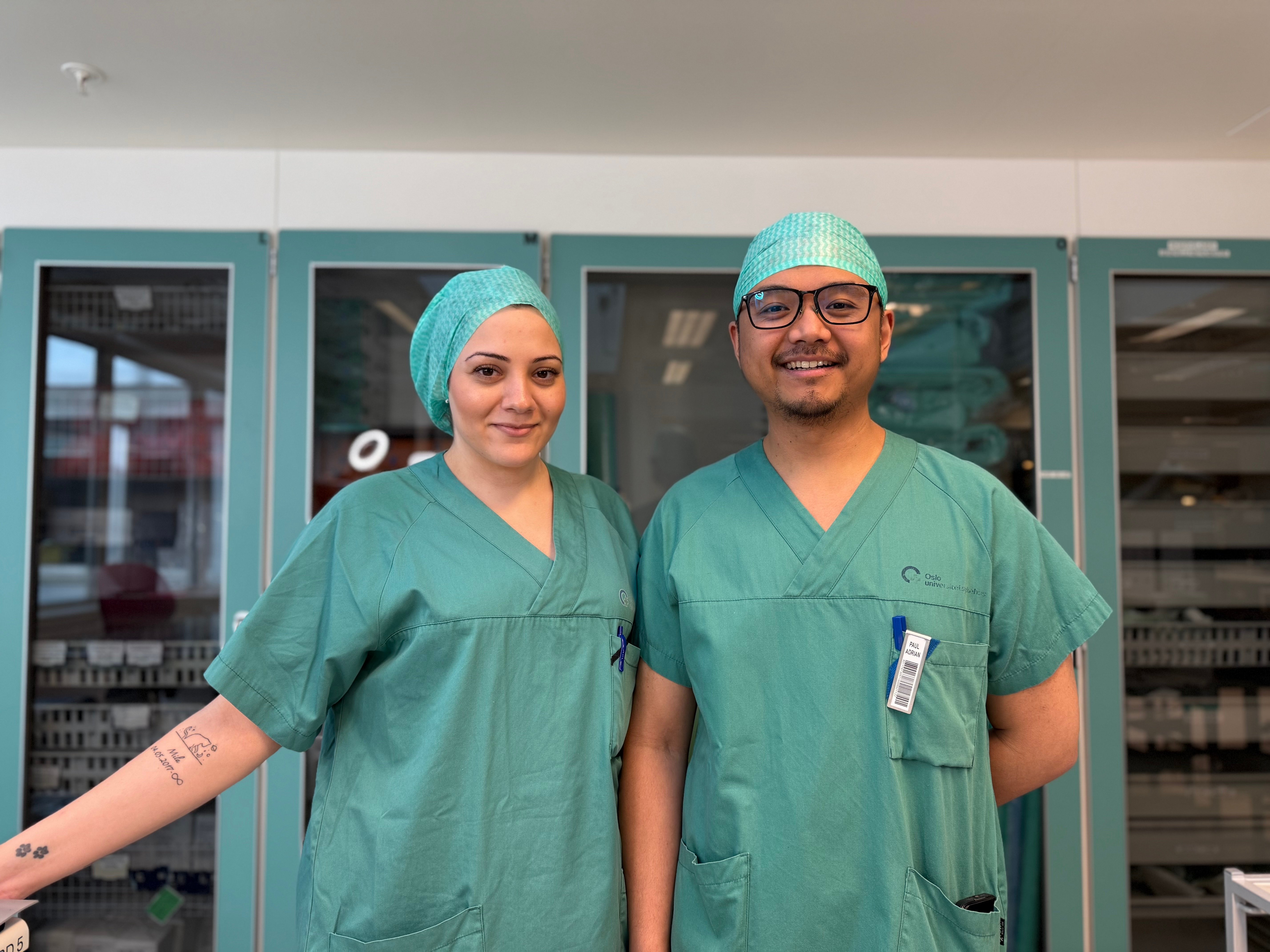 En mann og kvinne iført kirurgiske skrubber og poserer for et bilde