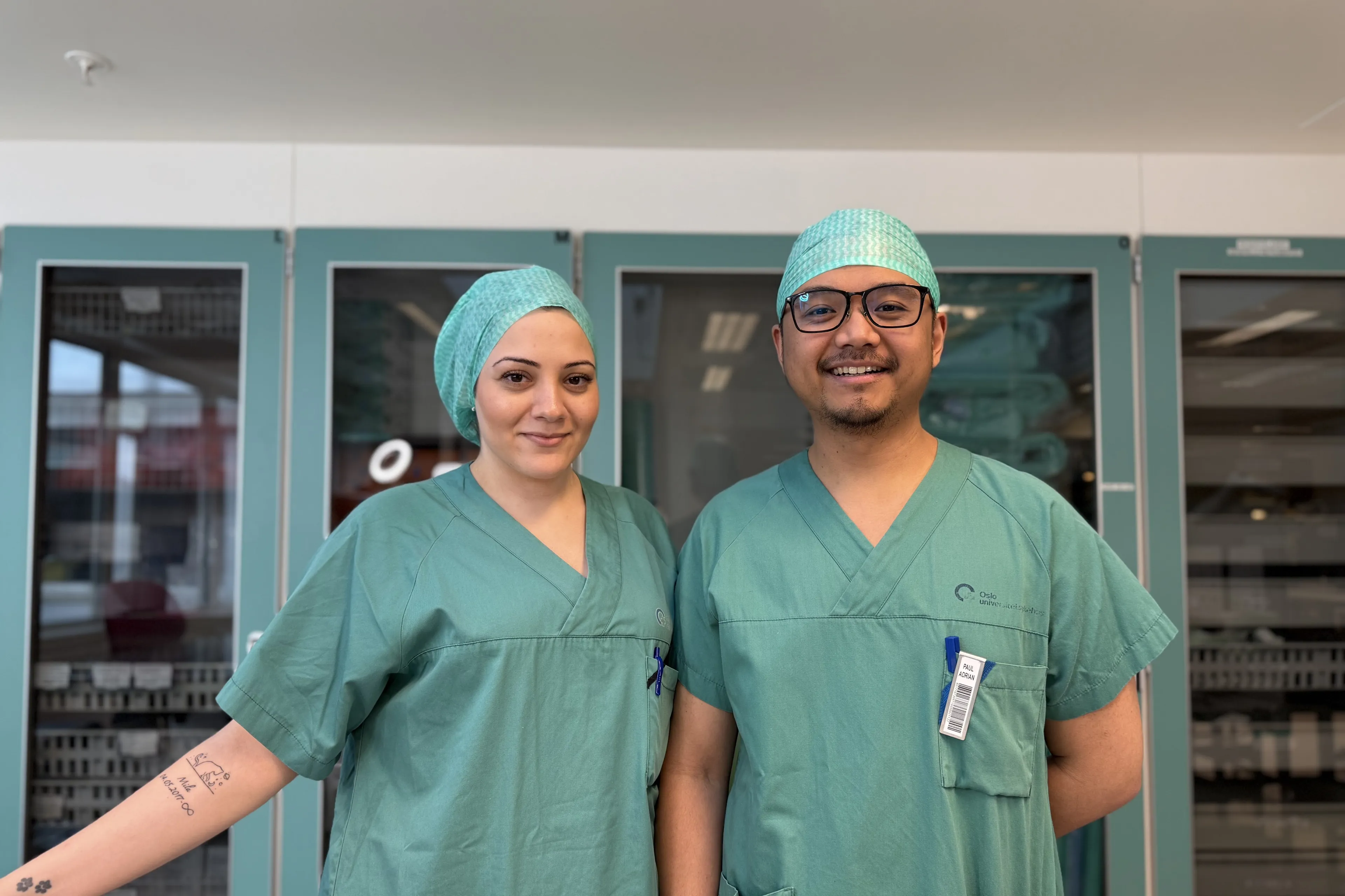 En mann og kvinne iført kirurgiske skrubber og poserer for et bilde