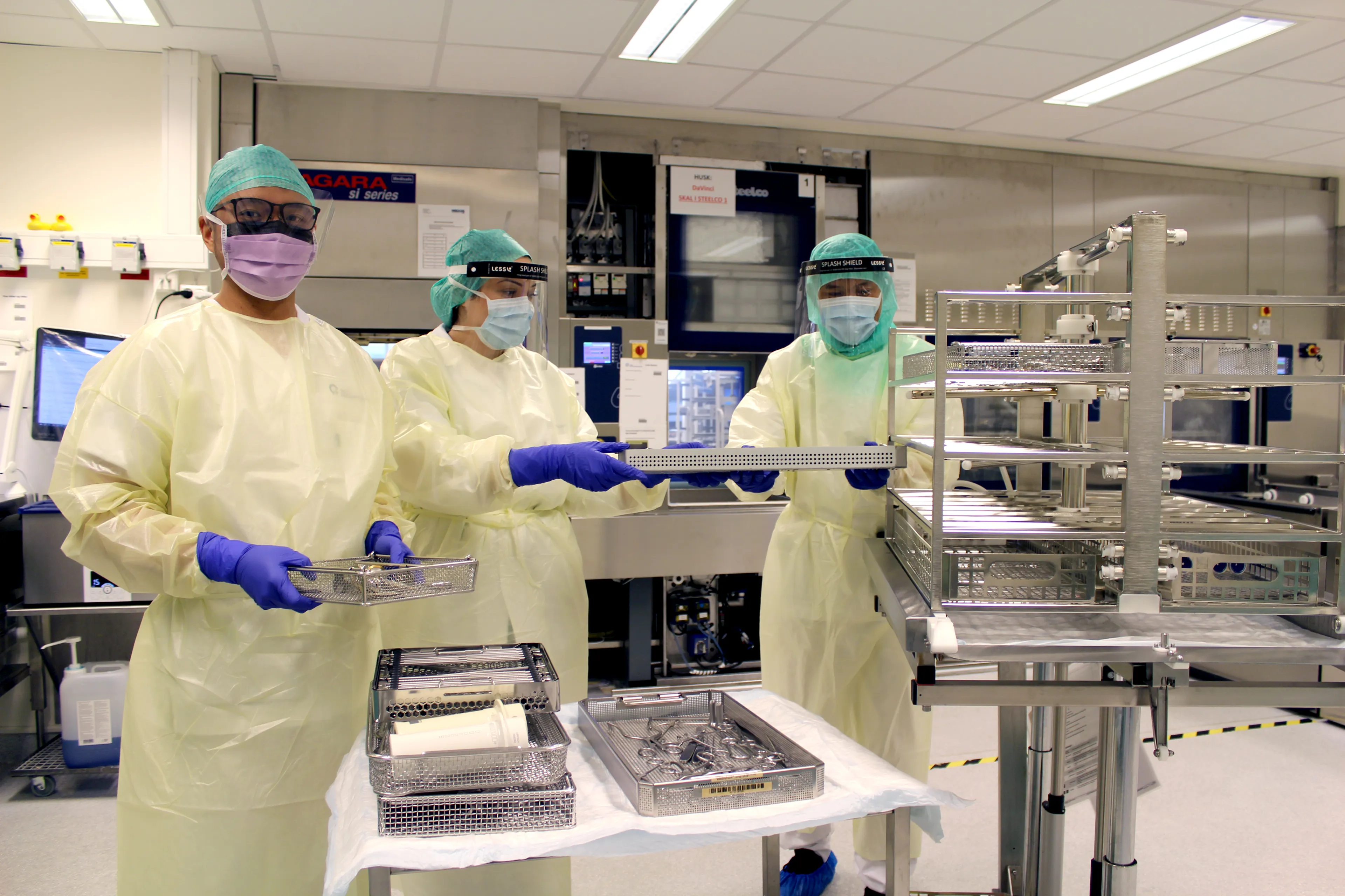 Bilde av tre helsepersonell i steril uniform som jobber med å sterilisere utstyr.