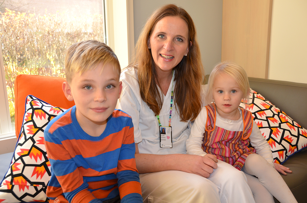 Gutt og jente sitter i sofa sammen med sykepleier i hvit uniform