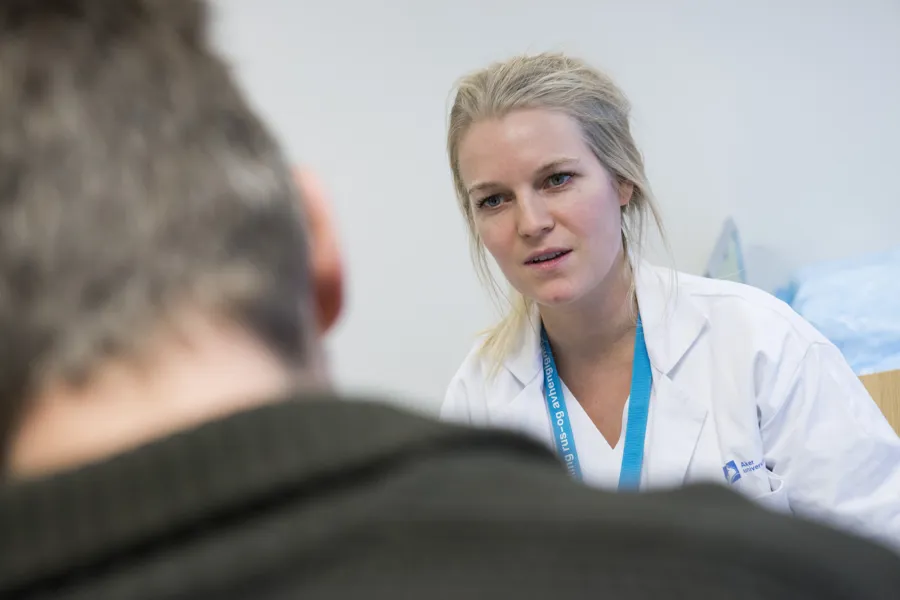 Kvinne i hvit sykehusuniform i samtale med mann
