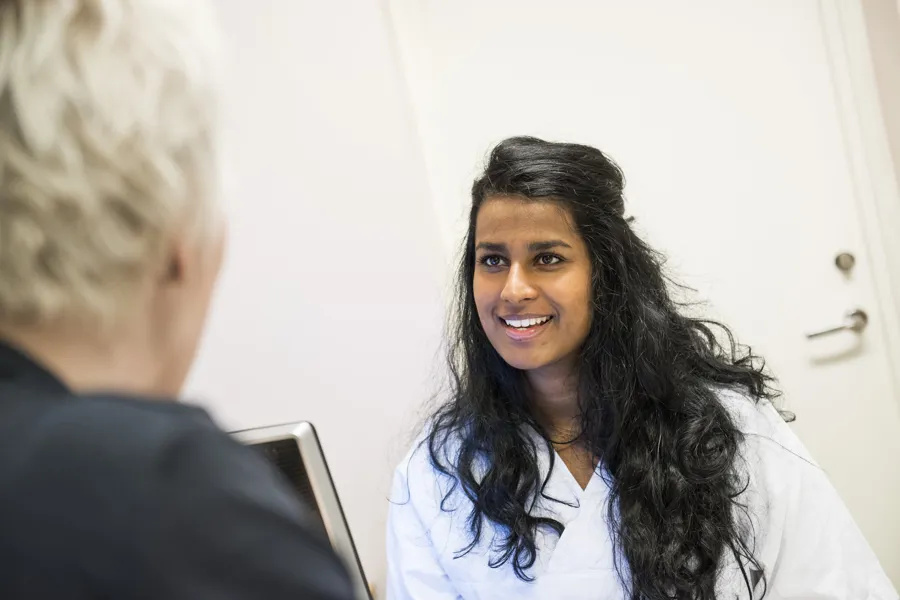 Kvinne i hvitt sykehustøy snakker med pasient