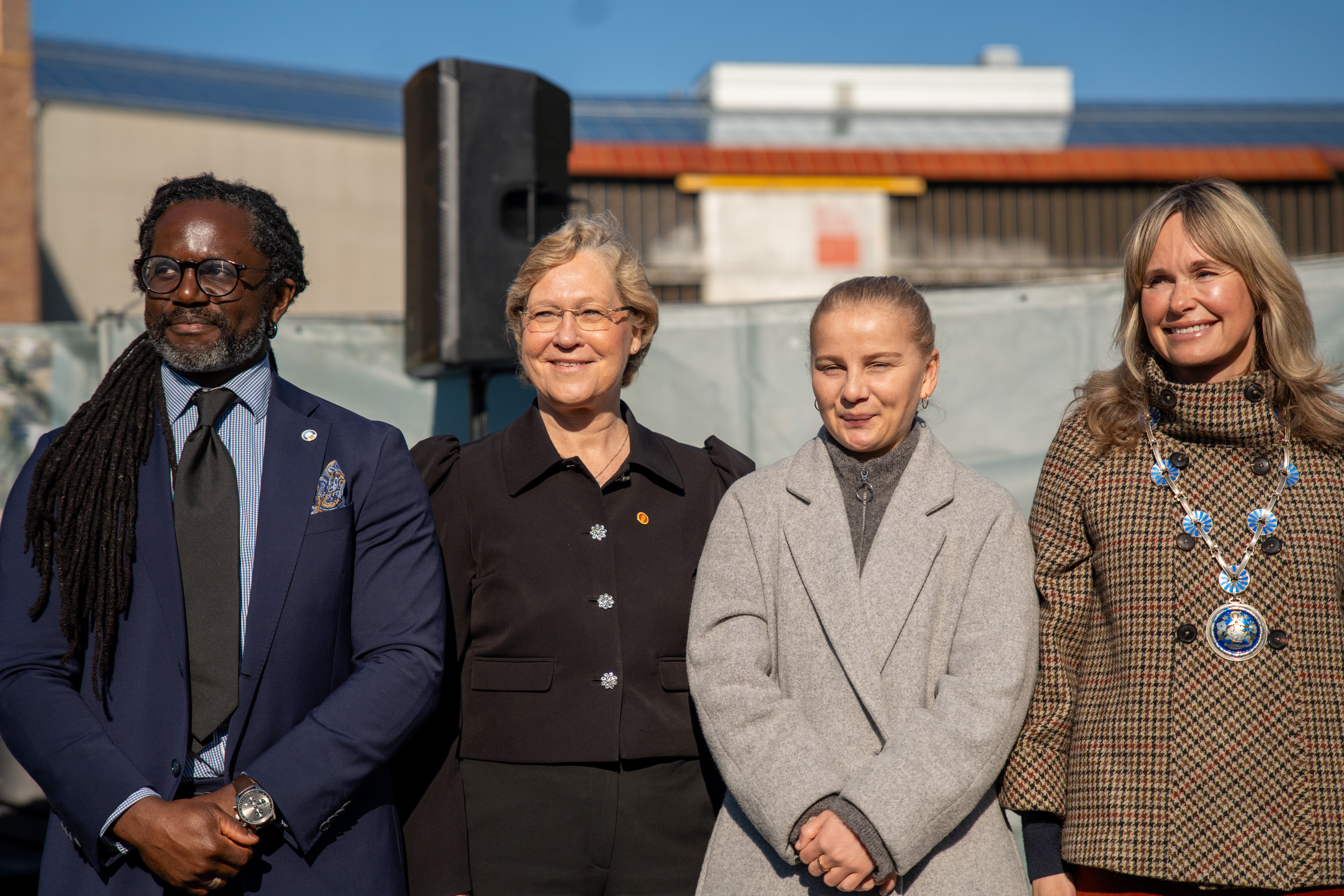 Fire mennesker står ved siden av hverandre og smiler i sola.