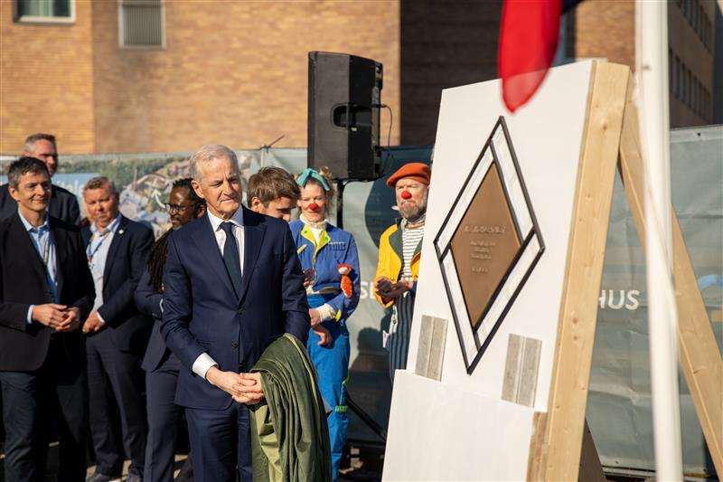 En gruppe mennesker og statsminister Jonas Gahr Støre står og ser på grunnsteinen.