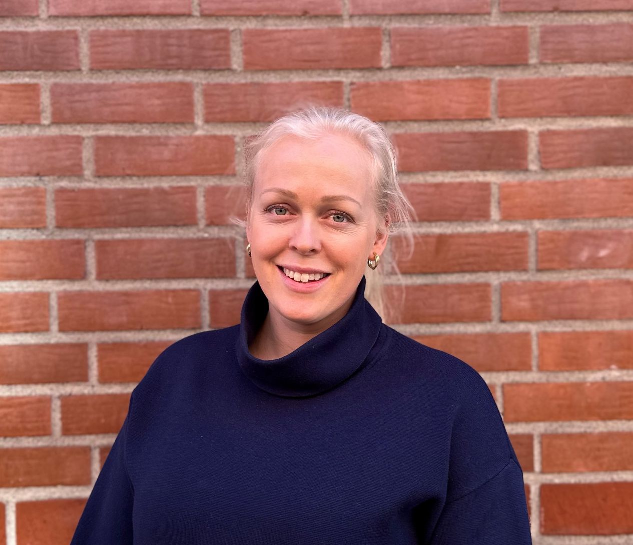 En person som smiler foran en murvegg