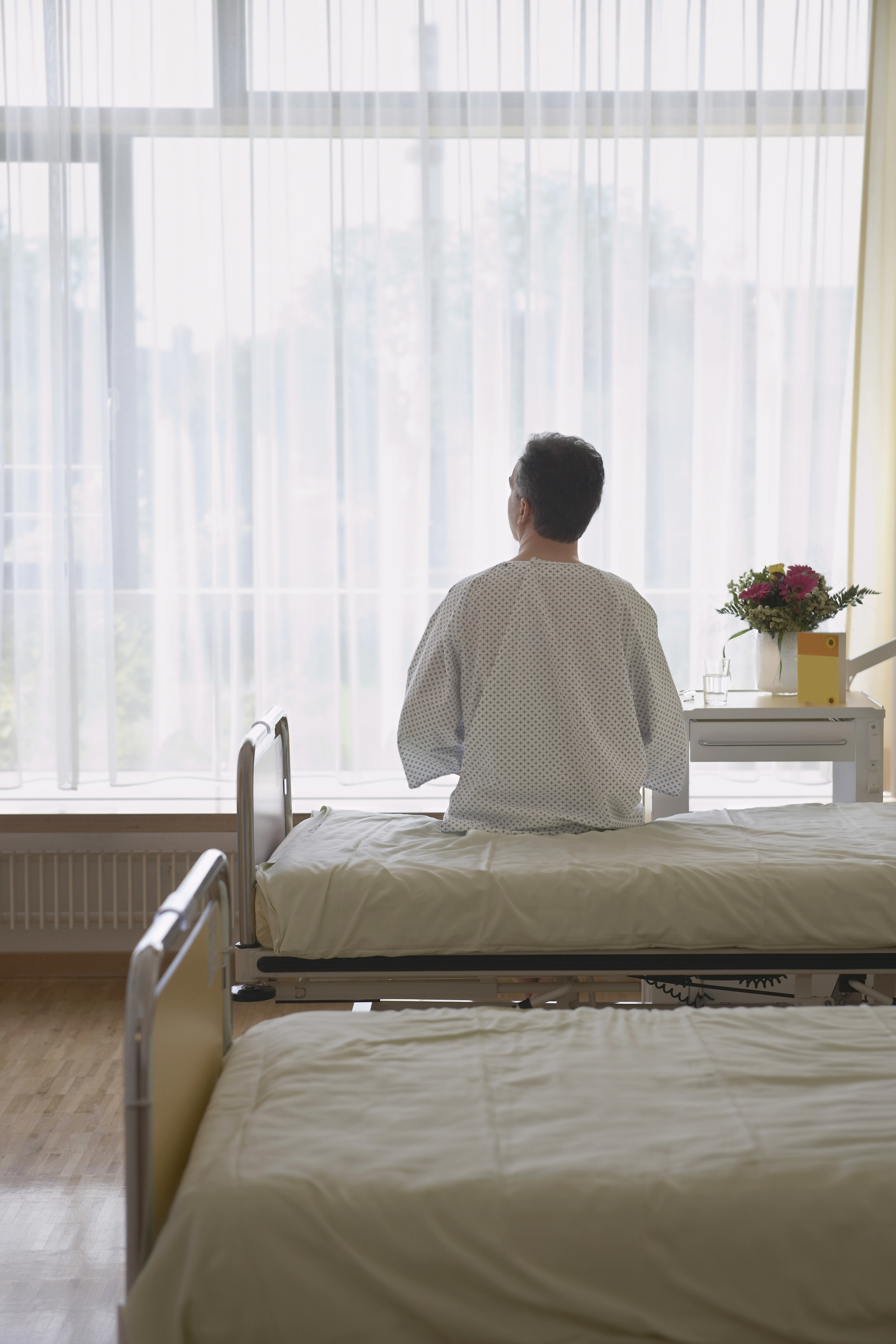 En pasient som sitter på en seng med ryggen mot oss og ser ut av vinduet