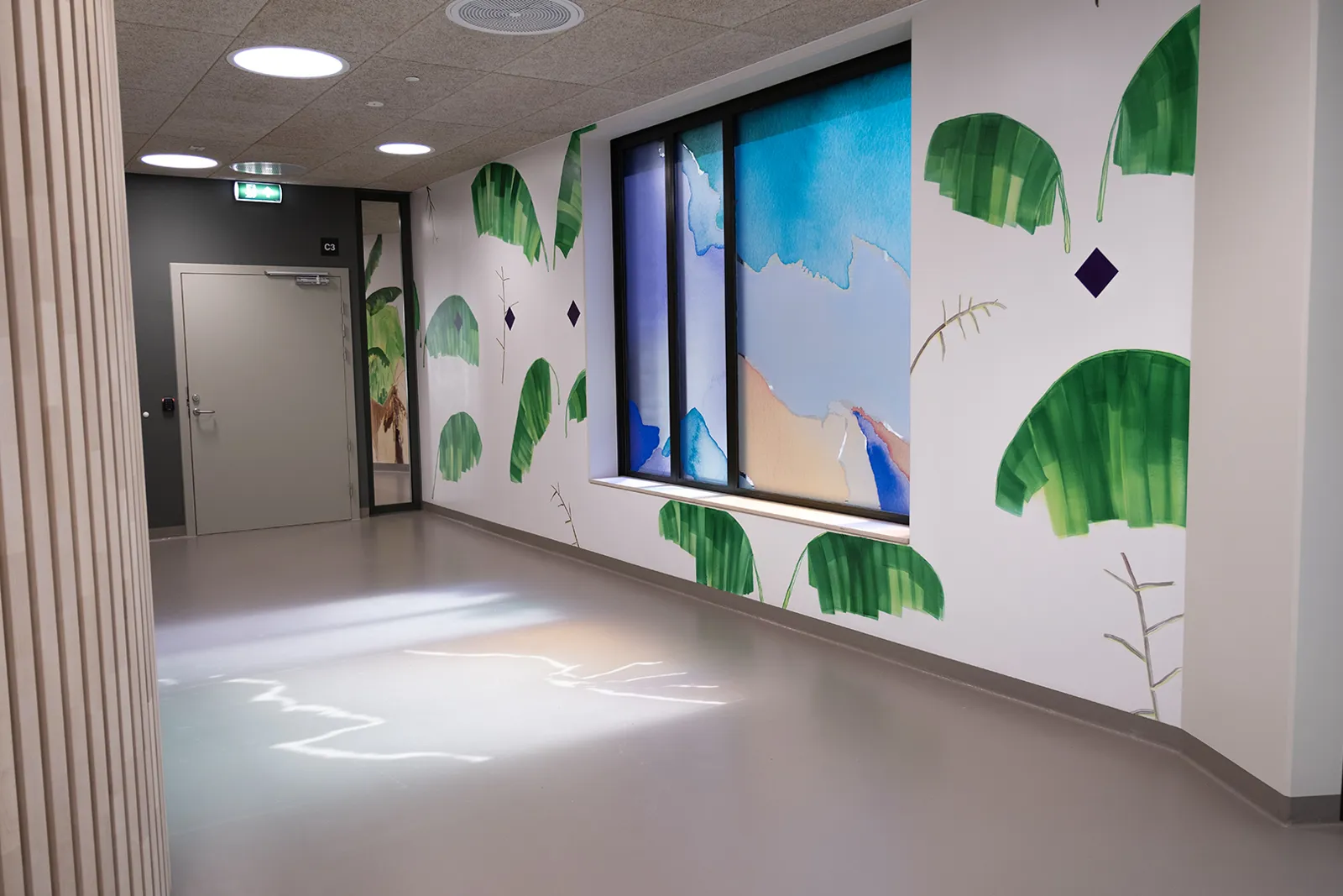 Veggmaleri av skog flere meter langt som også brer seg over foliering av vinduet, lyset skinner gjennom vinduet og lager refleksjon på gulvet.