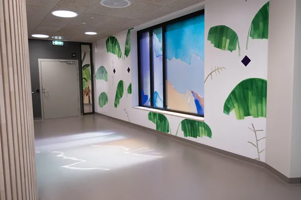 Veggmaleri av skog flere meter langt som også brer seg over foliering av vinduet, lyset skinner gjennom vinduet og lager refleksjon på gulvet.