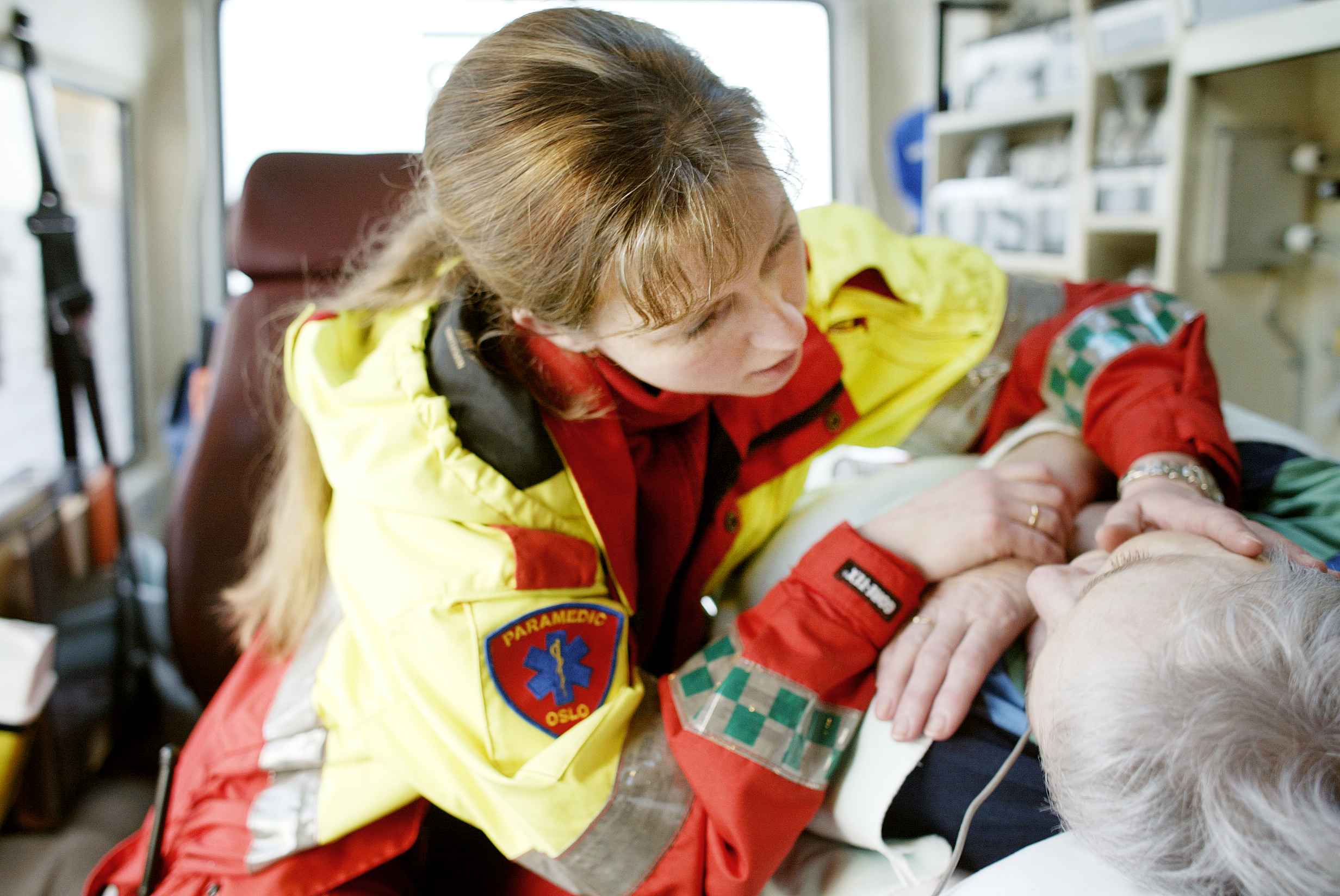 En paramedic i en ambulanse holder hånden sin på kinnet til en pasient som ligger på en båre inne i ambulansen.