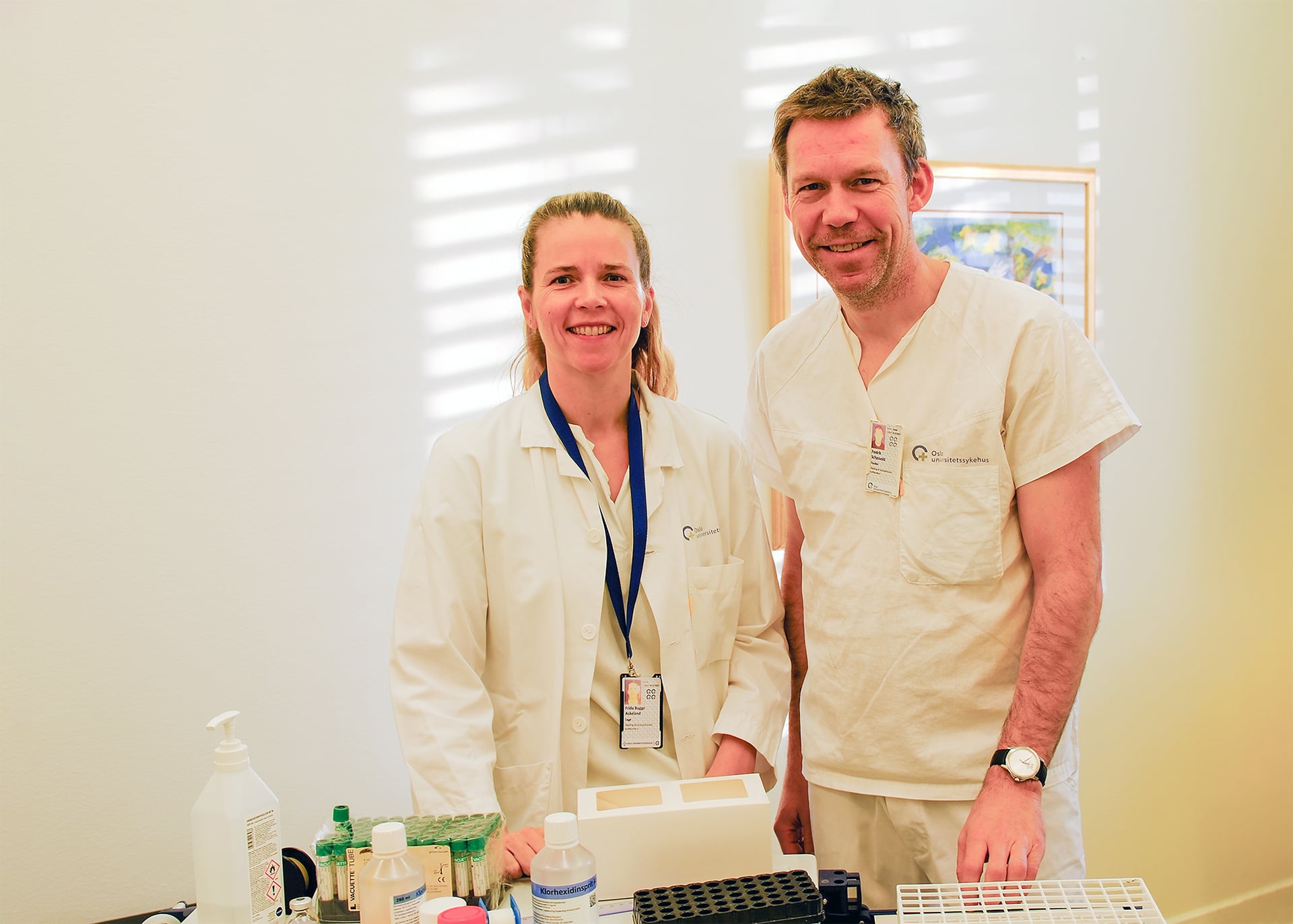 En mann og en kvinne i laboratoriefrakker står ved siden av en datamaskin