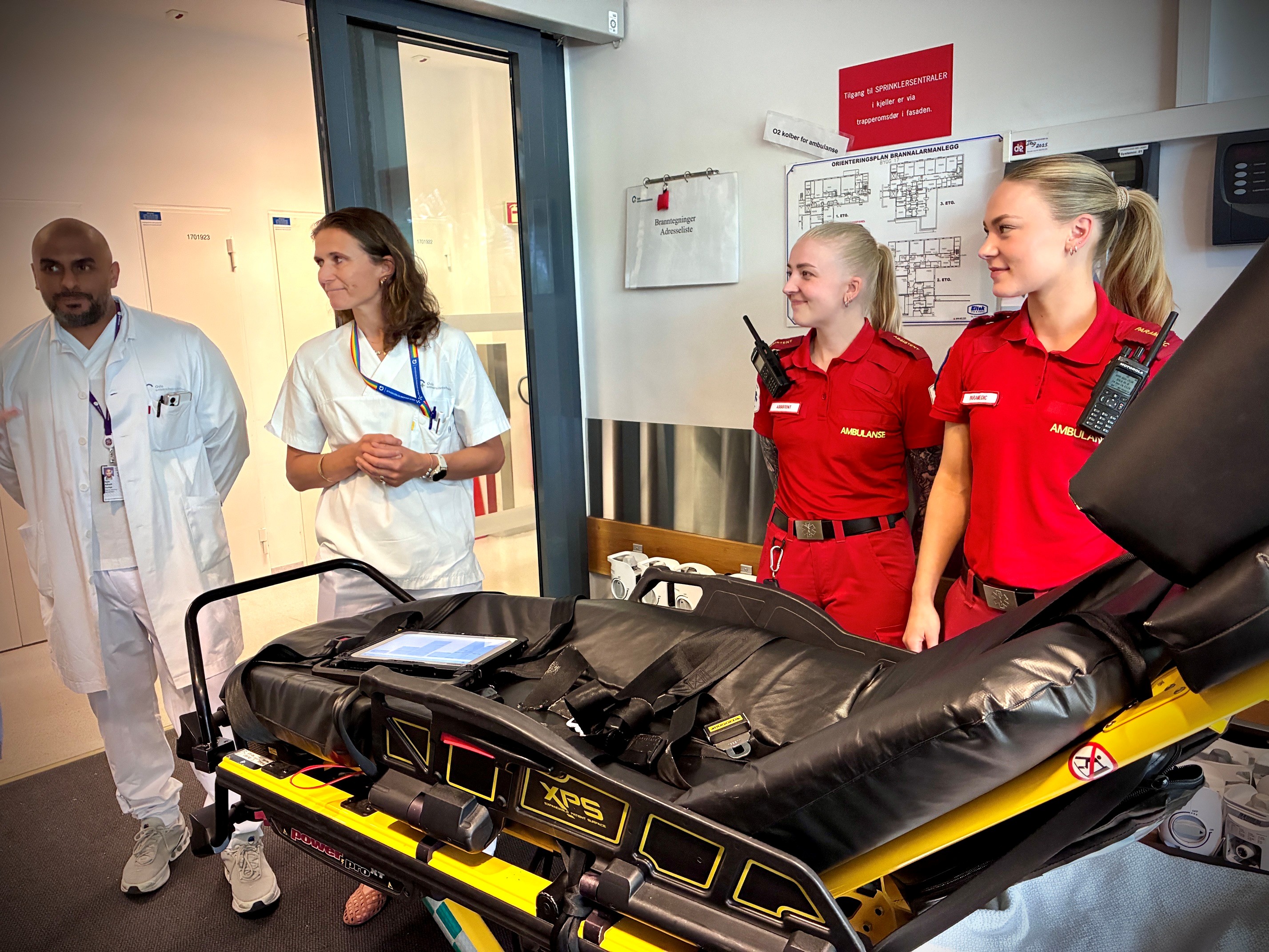 To paramedics og to helsepersonell står foran en båre.