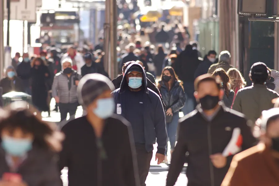 En gruppe mennesker som går nedover en gate med munnbind