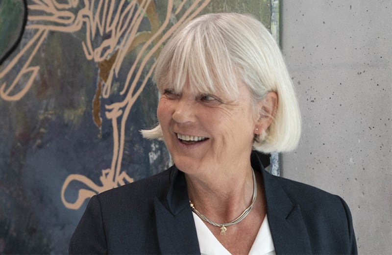 En dame som smiler foran en vegg med et maleri