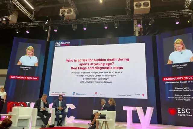 A group of people sitting on a stage with a large screen behind them