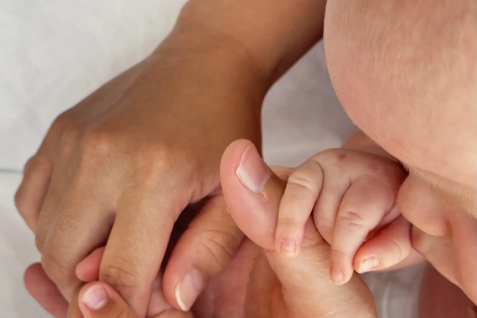 Et nærbilde av en babys hender som holder en babys hånd