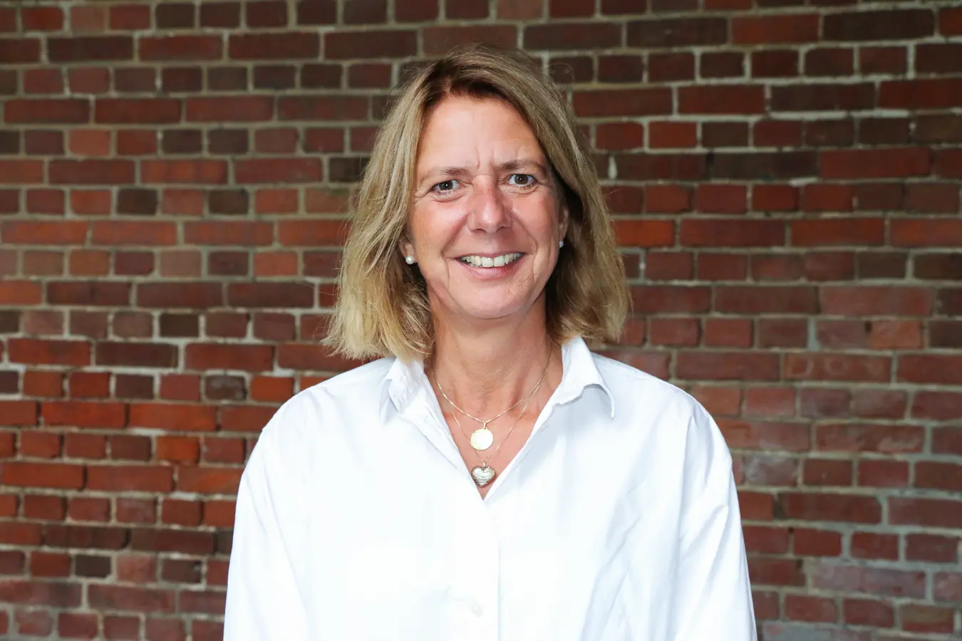 En person som smiler foran en murvegg