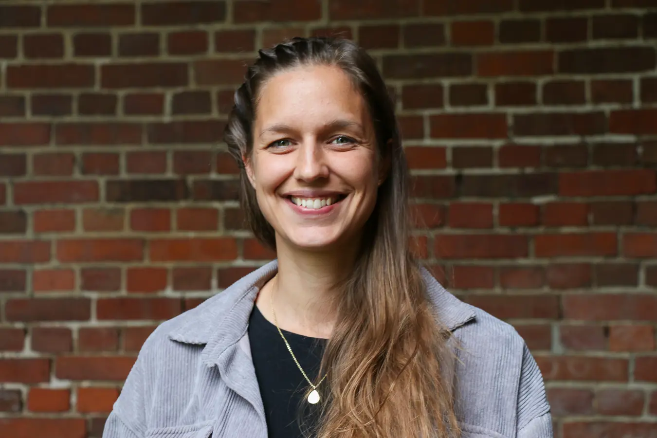 En person som smiler foran en murvegg