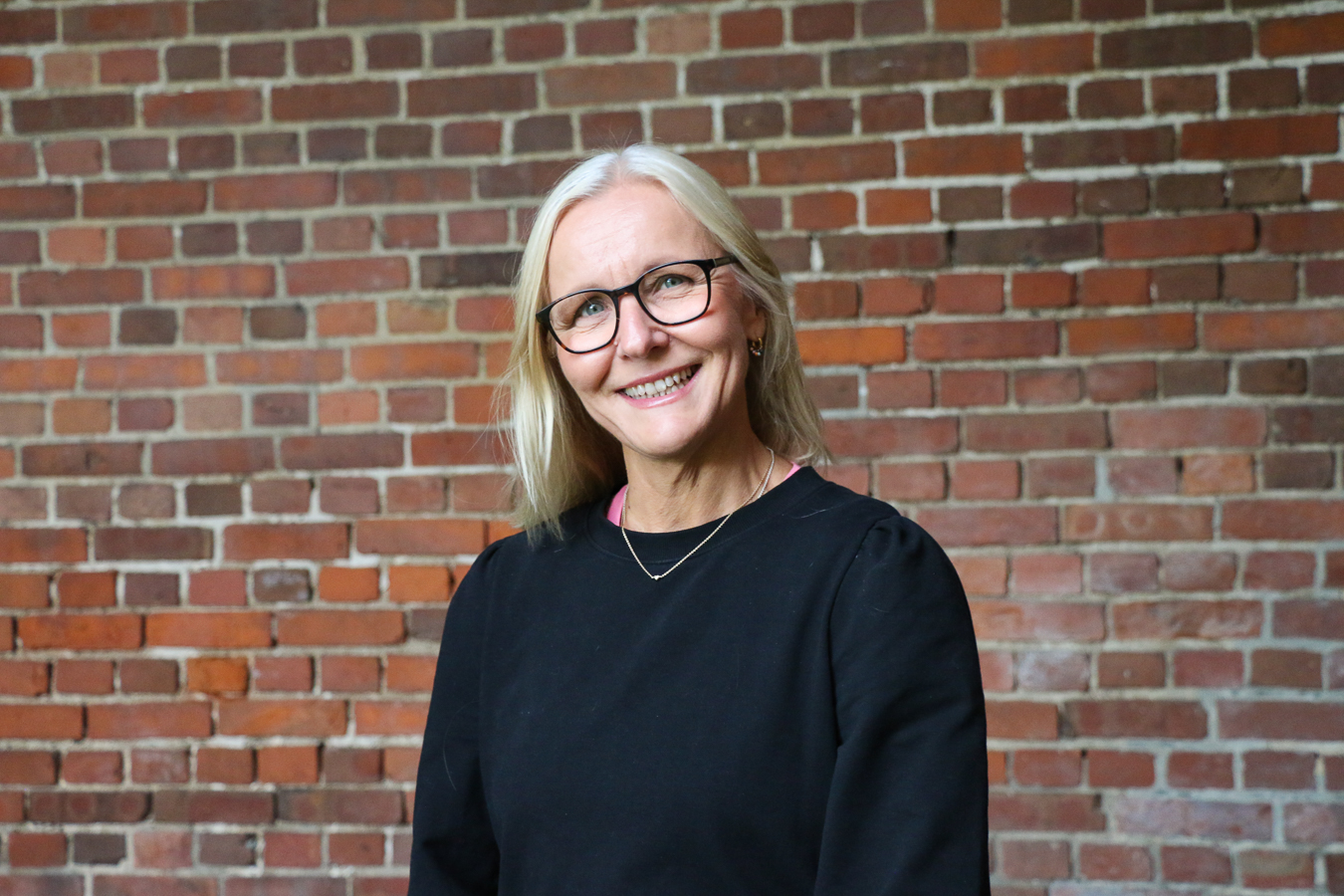 En person som smiler foran en murvegg