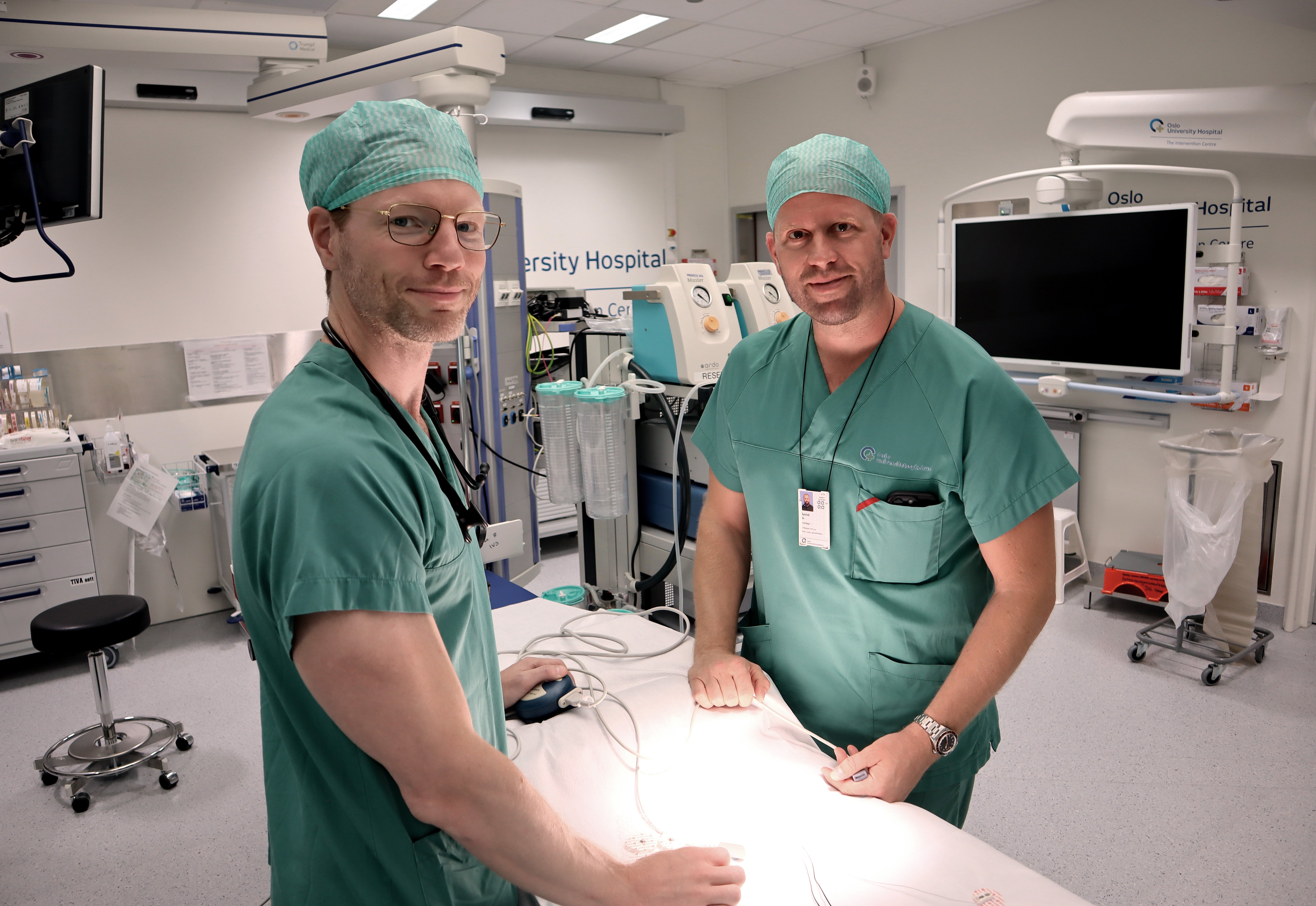Et par personer i kirurgiske uniformer i et rom med datamaskiner