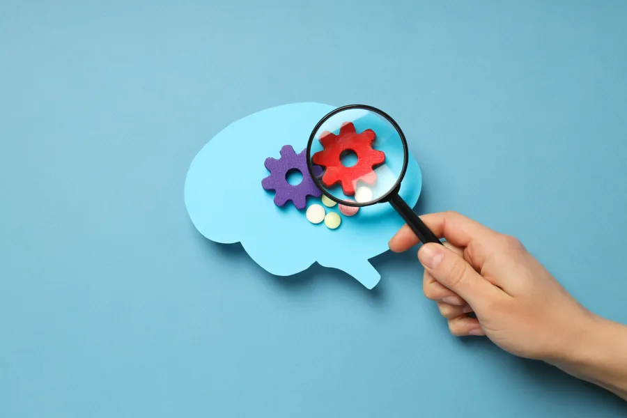 Hjerne fylt med tannhjul, som inspiseres med forstørrelsesglass