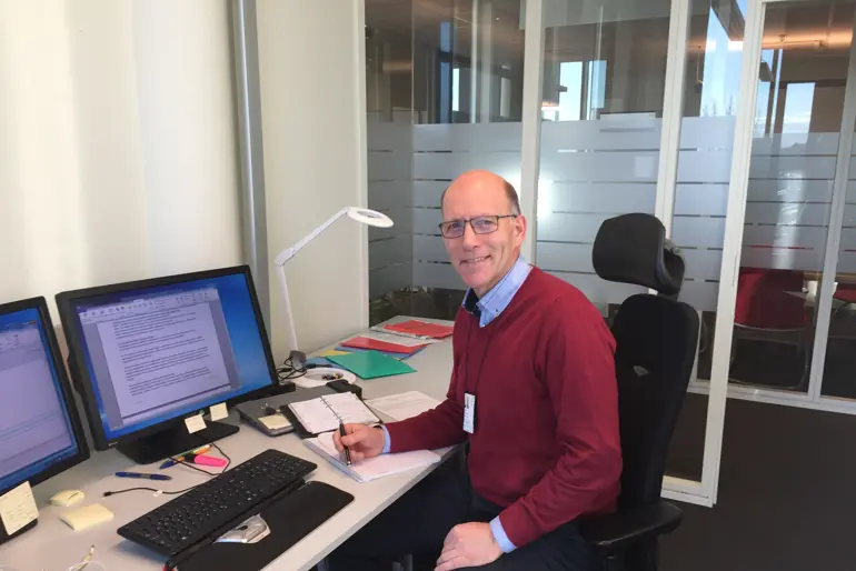 En mann som sitter ved et skrivebord med en datamaskin og et tastatur
