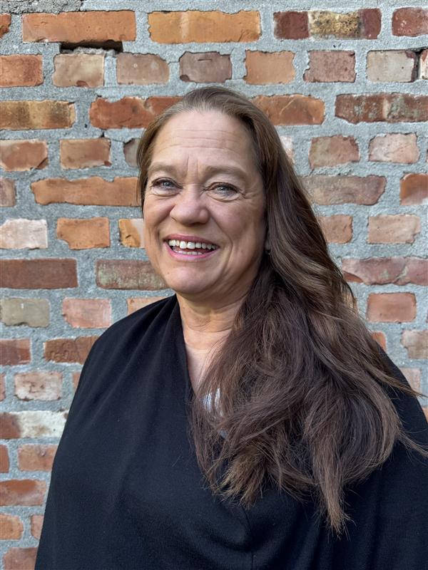 En person som smiler foran en murvegg