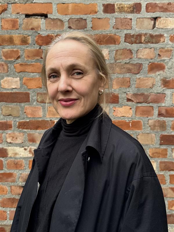 En kvinne som smiler foran en murvegg