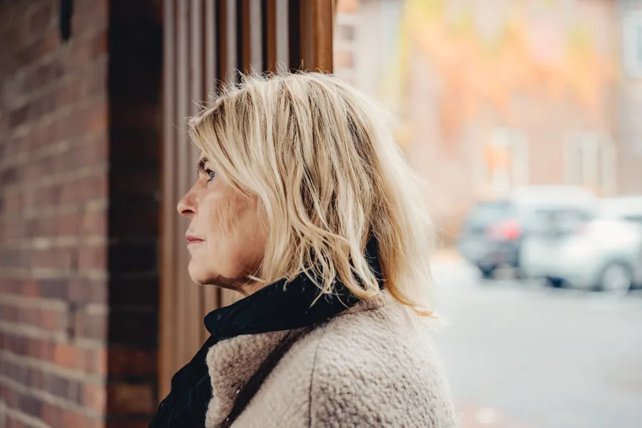 Eldre kvinne som står utendørs og ser ut i luften med et tankefullt ansiktsuttrykk