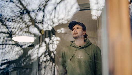 Mann står innendørs og ser ut av et vindu med et tankefullt ansiktsuttrykk.
