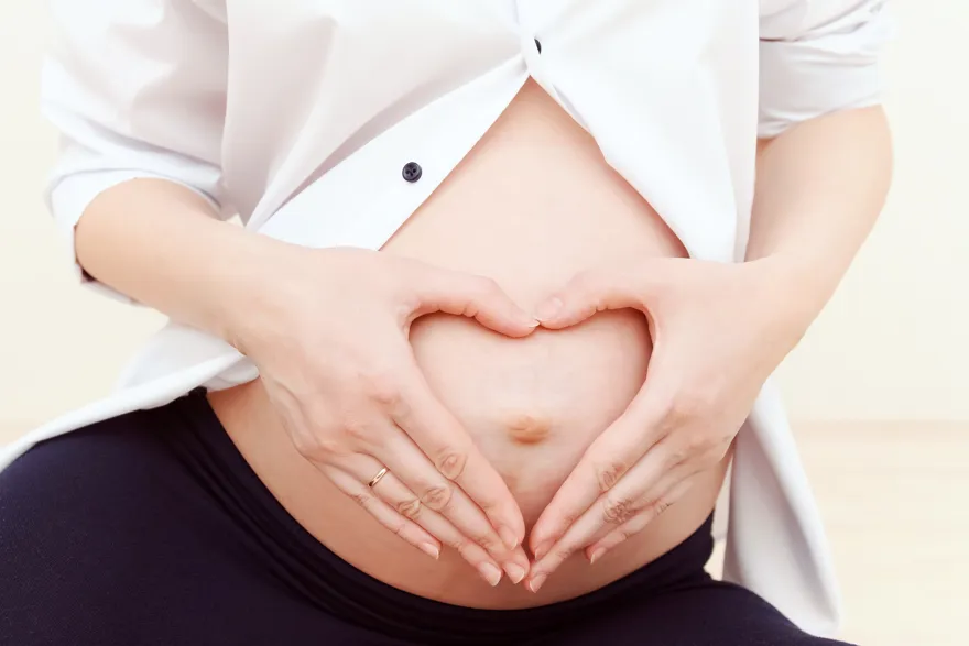 Gravid mage med hender formet som hjerte