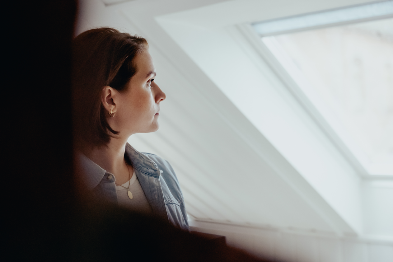 Ung kvinne med et alvorlig ansiktsuttrykk som ser ut av skråstilt takvindu.