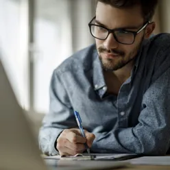 Mann sitter ved sin laptop og tar notater