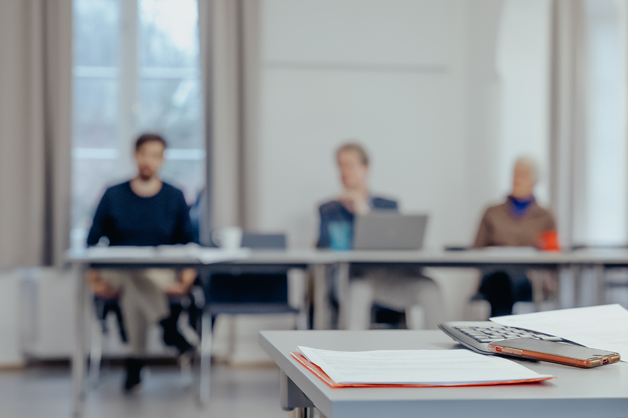 Tre personer sitter i en opplæringssituasjon. Foran i bildet ligger en mobiltelefon, et tastatur og en skriveblokk.