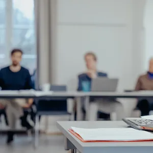 Tre personer sitter i en opplæringssituasjon. Foran i bildet ligger en mobiltelefon, et tastatur og en skriveblokk.